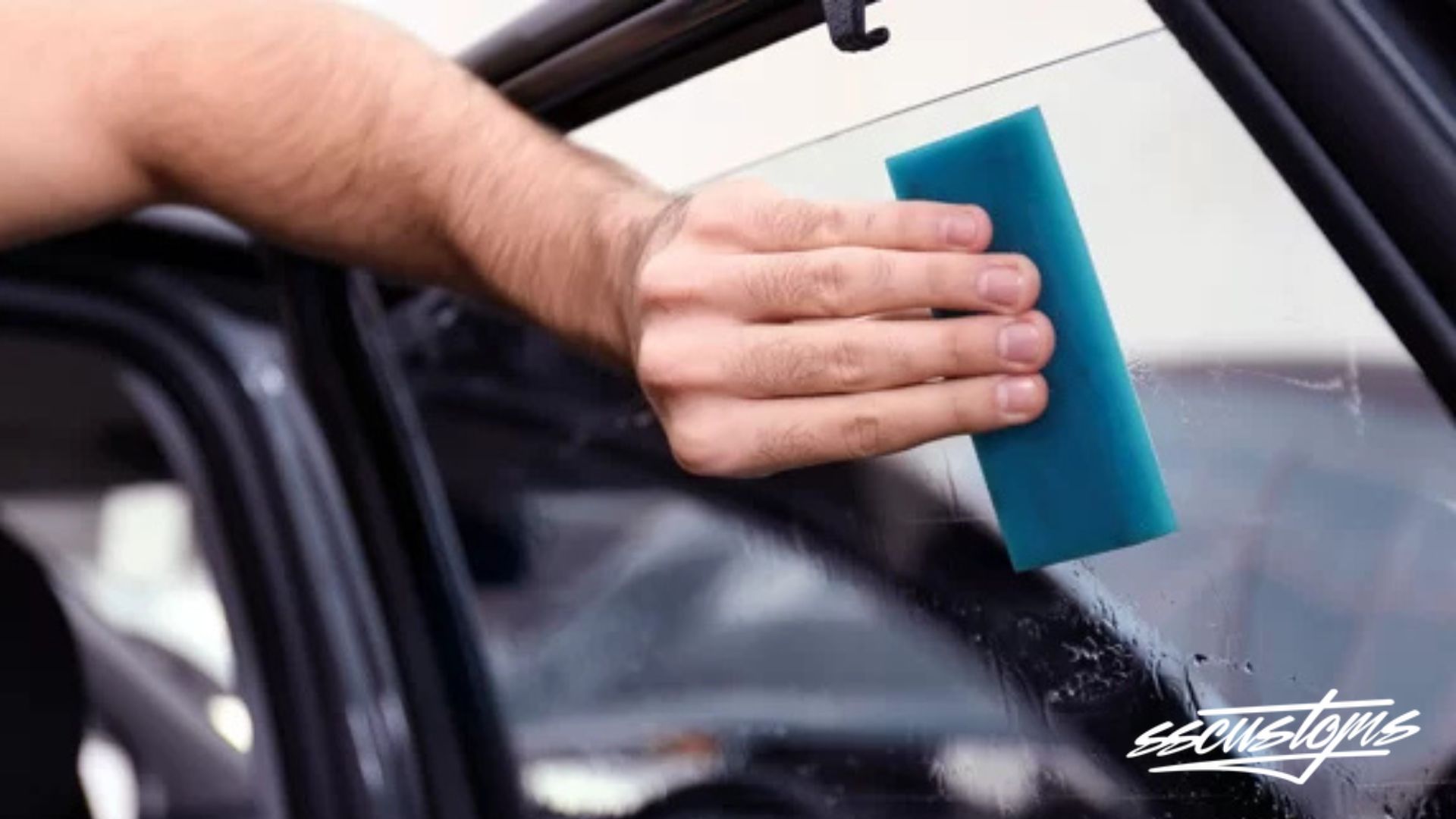 A technician smooths window tint onto a car window with a blue squeegee. The text “ezcustoms” appears in the bottom right corner.