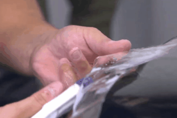 A close up of a hand applying clear paint protection film to a vehicle panel. The transparent film is being smoothed into place to help protect the car paint from scratches.